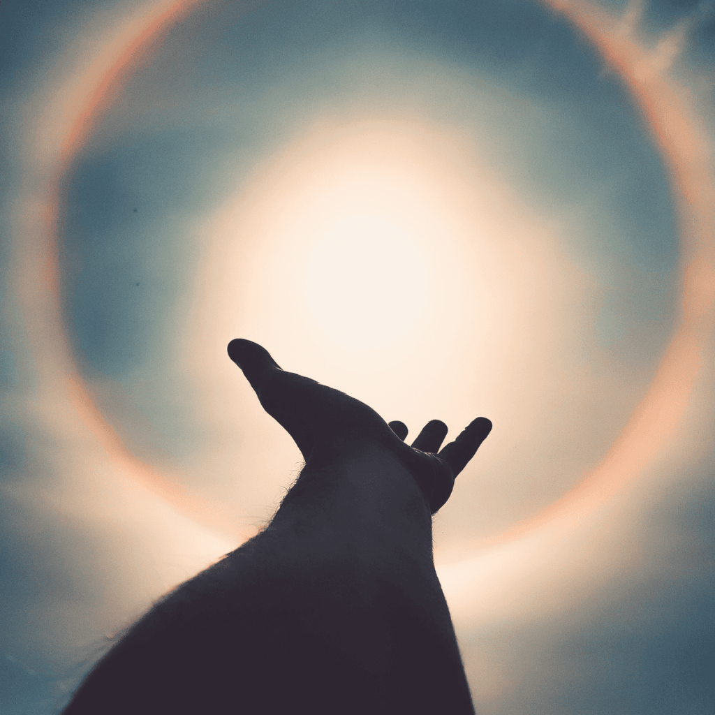 a picture of a hand that is in shadow reaching up towards the sun.