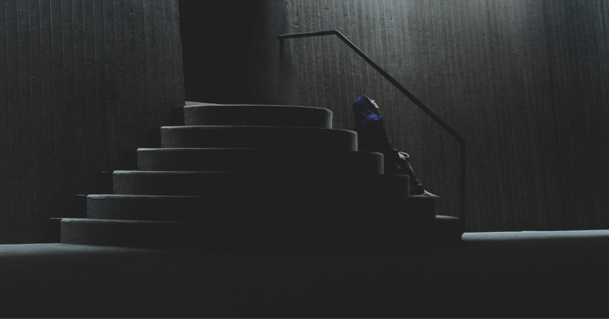 a picture of a man sitting on stairs outside a door, looking up at the sky in deep thought
