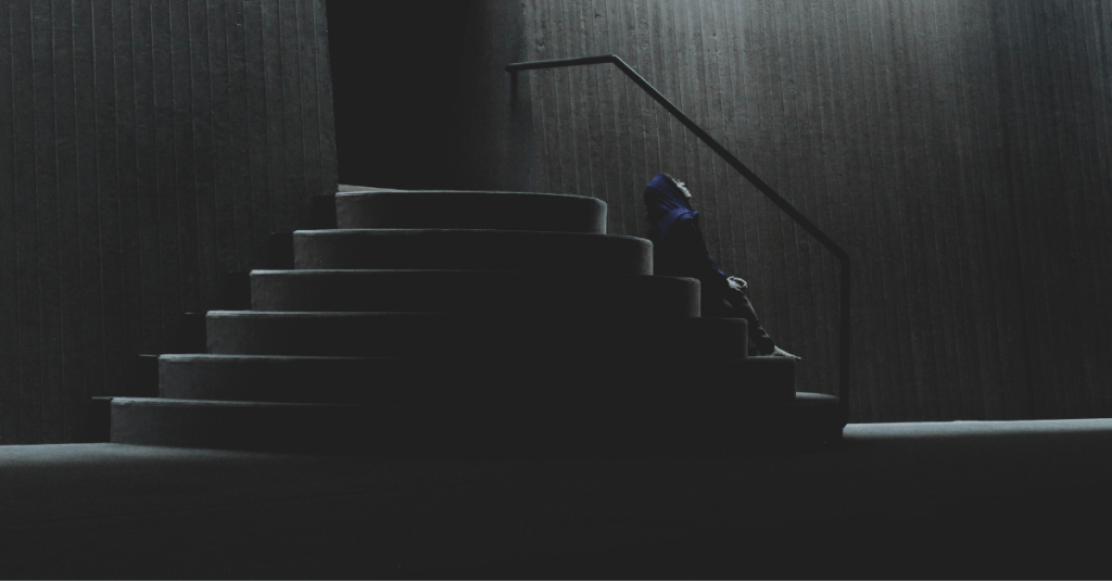 a picture of a man sitting on stairs outside a door, looking up at the sky in deep thought