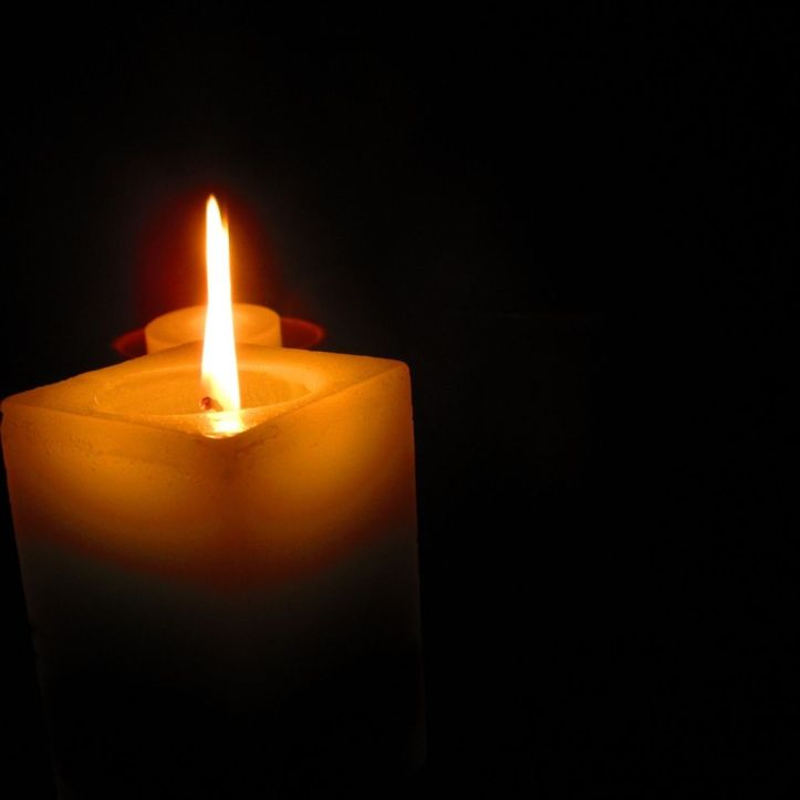 A dark room illuminated by soft light of a candle flame, used to symbolize and help reflect with a religious haiku illustrating faith in challenging moments
