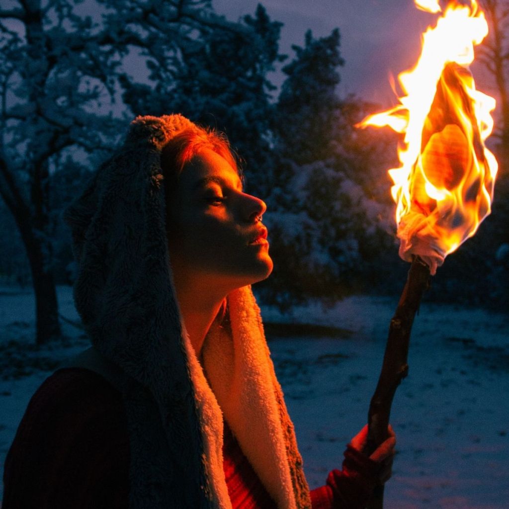 A woman carrying a torch in the night during winter, bathed by the soft light of the fire, symbolizing a Christian haiku about trusting God in hard times or even when you can't see the road ahead.