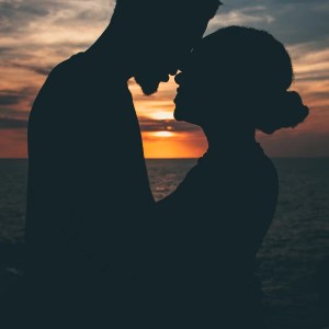 a silhouette of two lovers on a beach next to the ocean with a sunset in the background. It's a supporting image for a rhyming love poem about deep, unconditional love in relationships.