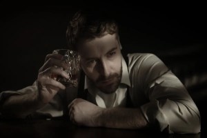 man with glass of whiskey in the dark looking helpless and depressed because he can't stop stop drinking