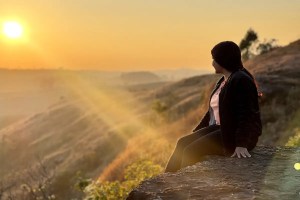 a woman sits in the rays of the sun in the morning on a hill